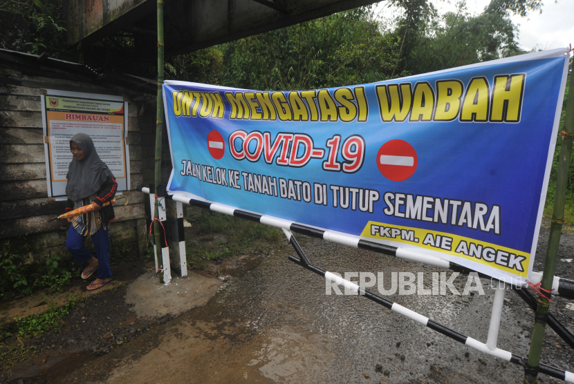 Warga melintas di samping portal yang menutup akses ke desa di Nagari Aia Angek, Kabupaten Tanah Datar,  Sumatera Barat, Jumat (17/04/2020). Warga menutup sejumlah akses masuk ke desa di daerah itu bagi pendatang untuk mencegah penyebaran COVID-19
