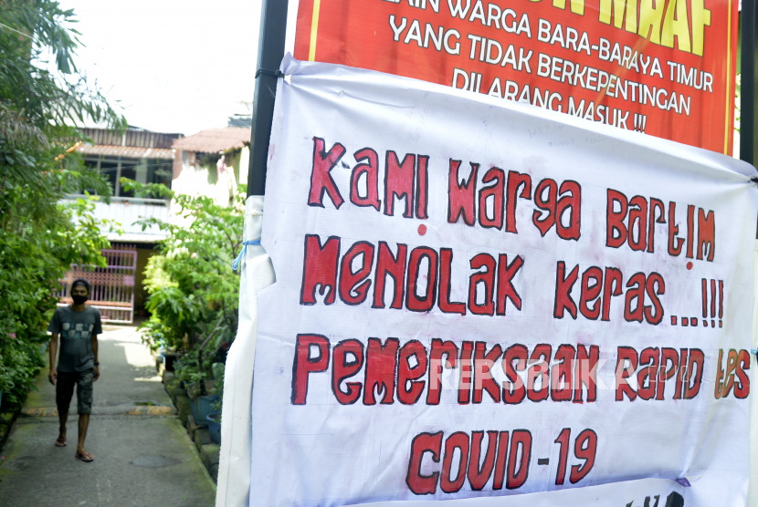 Warga berjalan di dekat spanduk penolakan mengikuti tes diagnostik cepat (Rapid Test) COVID-19 di Makassar, Sulawesi Selatan. Kampus Unhas terus berusaha mencari solusi penanganan Covid-19 di Sulawesi Selatan.