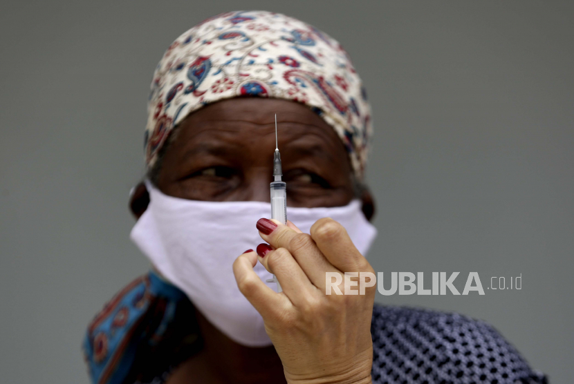 Regulator Kesehatan Brasil Tolak Vaksin Sputnik. Seorang petugas kesehatan memegang jarum suntik vaksin Sinovac untuk COVID-19 saat seorang wanita menunggu untuk mendapatkan suntikan pertamanya di quilombo Kalunga Vao de Almas di pinggiran Cavalcante, negara bagian Goias, Brasil, Selasa, 16 Maret 2021.