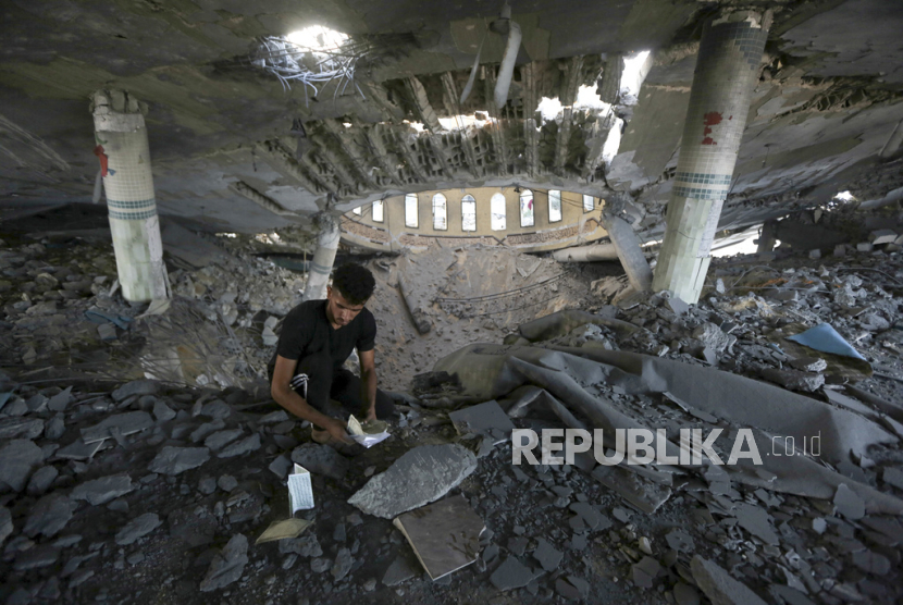 Seorang pria melihat buku-buku rusak di dalam masjid yang hancur akibat serangan udara Israel di Khan Younis, Jalur Gaza, Minggu, 8 Oktober 2023.
