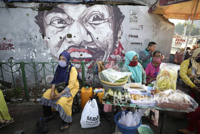 Perempuan memakai masker sebagai antisipasi wabah virus corona duduk di sebuah warung makan dekat mural di Jakarta, Indonesia, Senin, 21 September 2020. 