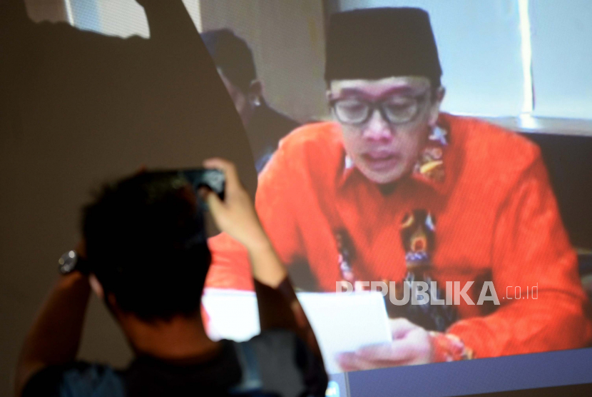 Jurnalis mengambil gambar layar yang menayangkan terdakwa mantan Menteri Pemuda dan Olahraga Imam Nahrawi saat menjalani sidang lanjutan secara online di Gedung KPK, Jakarta, Jumat (19/6). Sidang tersebut beragendakan pembacaan nota pembelaan (pledoi) terdakwa