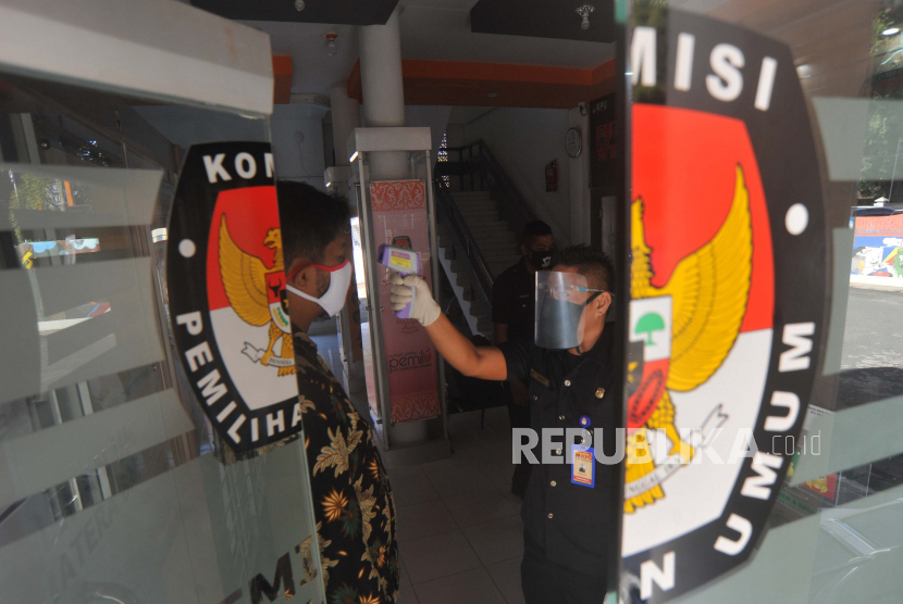 Petugas menggunakan pelindung wajah mengecek suhu tubuh staf yang datang di Kantor Komisi Pemilihan Umum (KPU) Sumatera Barat, di Padang. 