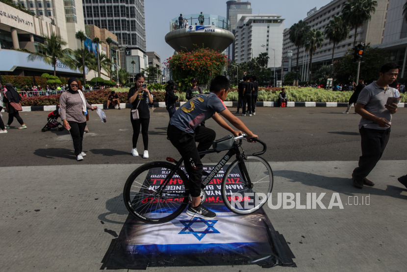 Pesepeda melintasi spanduk bergambarkan Bendera Israel saat Hari Bebas Kendaraan Bermotor di kawasan Bundaran HI, Jakarta, Ahad (12/11/2023). Aksi tersebut sebagai bentuk solidaritas untuk masyarakat Palestina yang masih dilanda konflik perang dengan Israel.