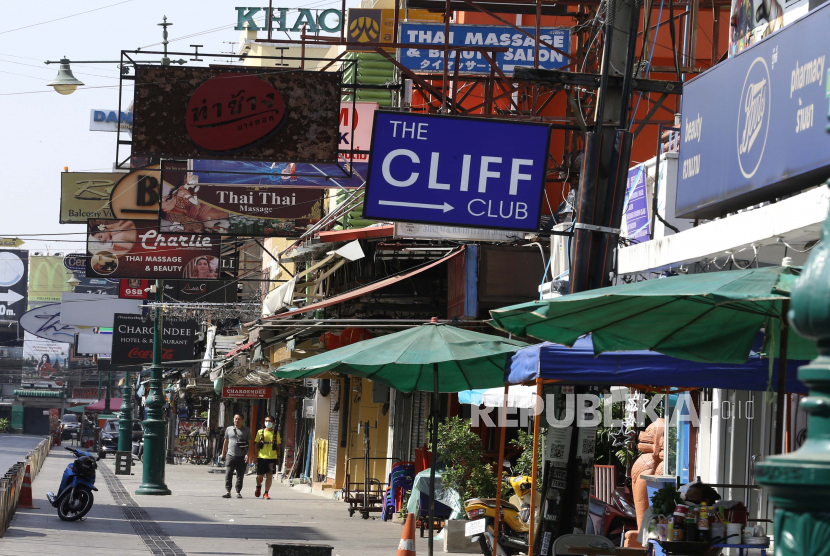 Orang-orang berjalan melewati toko-toko yang tutup di tempat wisata yang hampir sepi di Jalan Khaosan di Bangkok, Thailand, Selasa (12/1).