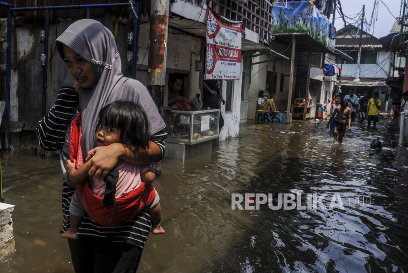 Seorang warga menggendong anaknya saat terjadi banjir rob di Jakarta. (Ilustrasi