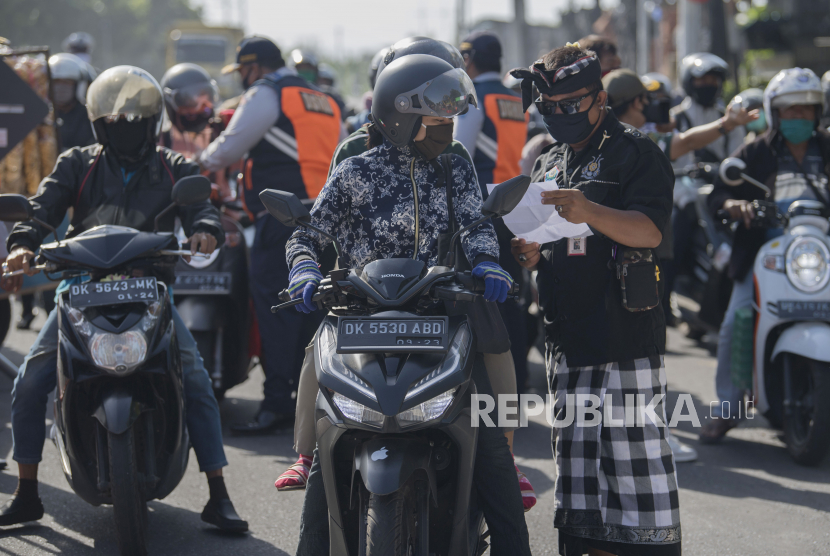 Anggota satuan pengamanan adat Bali atau Pecalang memeriksa surat jalan seorang pengendara saat hari pertama penerapan Pembatasan Kegiatan Masyarakat (PKM) di pos pantau perbatasan Biaung, Denpasar, Bali, Jumat (15/5/2020). Kota Denpasar menerapkan PKM selama satu bulan dengan mendirikan 10 pos pantau terutama di perbatasan kota untuk mengawasi aktivitas warga tanpa tujuan jelas dan melanggar protokol kesehatan termasuk melanggar larangan mudik dalam upaya menghentikan penyebaran wabah COVID-19