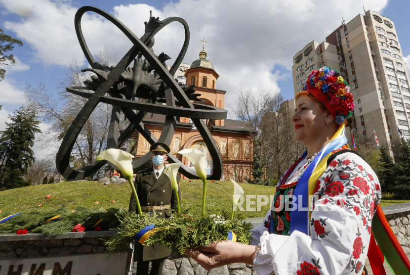 Seorang wanita dengan kostum rakyat Ukraina meletakkan bunga di monumen korban Chernobyl di ibu kota Kyiv, Ukraina, beberapa waktu lalu.