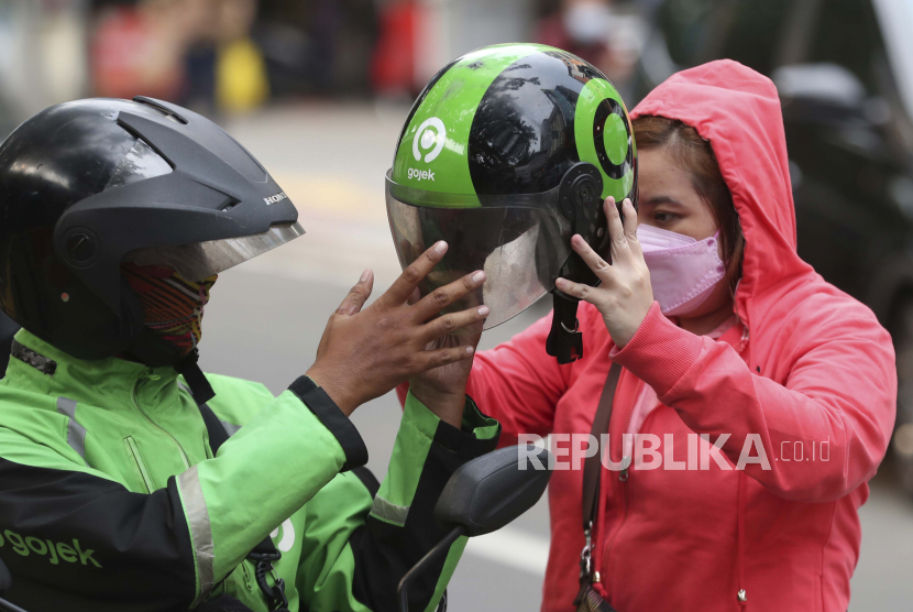 Seorang pengemudi ojek online memberikan helm kepada seorang pelanggan di Jakarta, Indonesia, Senin, 17 Mei 2021. Kementerian transportasi China memperketat regulasi yang mengatur perusahaan ride-hailing online atau platform penyedia jasa transportasi harus membagikan data mereka dengan regulator. 