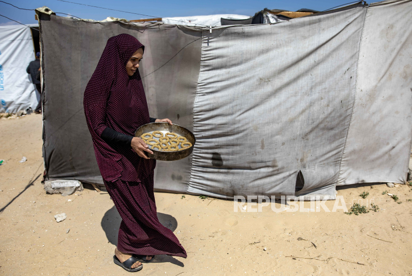 Seorang wanita Palestina membawa nampan makanan tradisional sebelum Idul Fitri, yang menandai akhir bulan suci Ramadhan, di dalam tenda di kamp Rafah di selatan Jalur Gaza, (9/4/2024). 