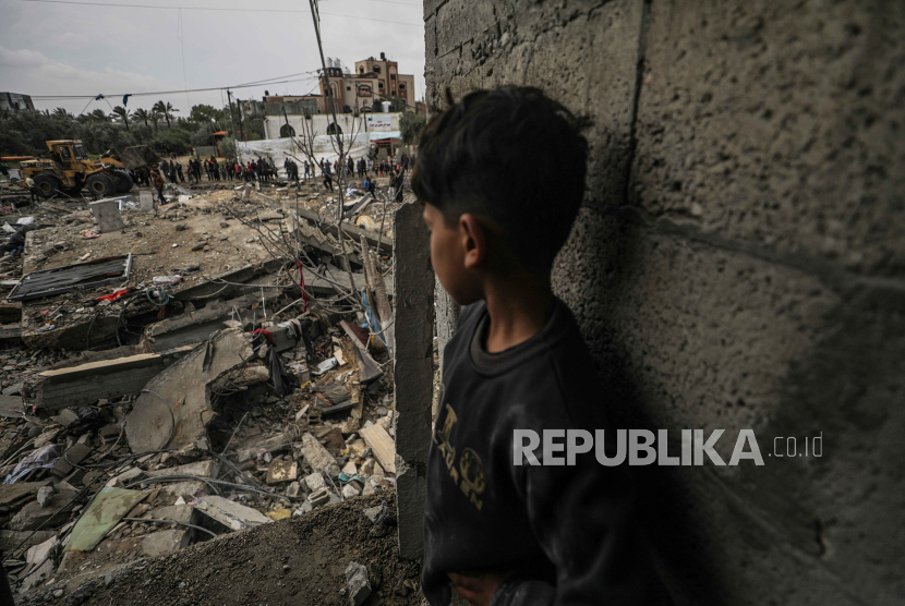 Seorang anak laki-laki menyaksikan warga Palestina mencari orang hilang di bawah reruntuhan rumah yang hancur akibat serangan udara Israel, di kamp pengungsi Al Nusairat, Gaza Selatan.
