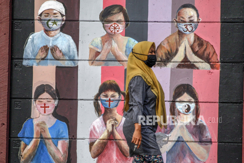 Warga melintas di dekat mural bergambar simbol orang berdoa menggunakan masker yang mewakili umat beragama di Indonesia 