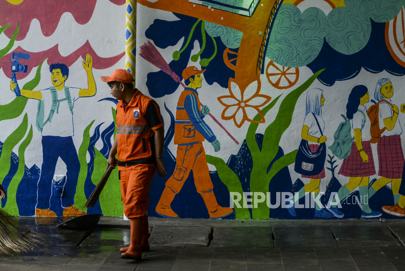 Petugas PPSU berjalan di dekat mural di Terowongan Kendal, Sudirman, Jakarta, Senin (27/6/2022). Mural bertemakan Jakarta Kota Global tersebut menampilkan ikon Kota Jakarta dan sarana fasilitas umum berstandar Internasional seperti JIS, MRT dan Formula E. Republika/Putra M. Akbar