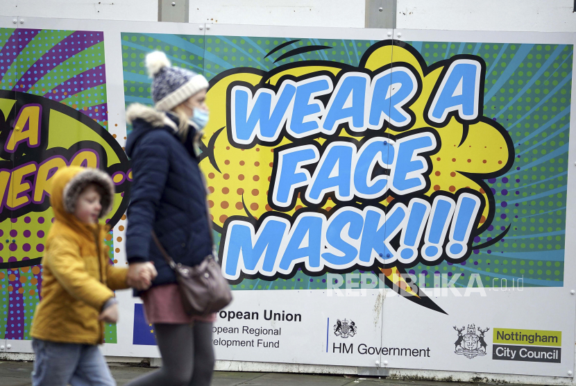  Orang-orang berjalan melewati papan reklame yang mengundang warga untuk memakai masker wajah untuk mengekang penyebaran COVID-19, di Nottingham, Inggris, Senin 20 Desember 2021. Direktur Jenderal Organisasi Kesehatan Dunia (WHO) Tedros Adhanom Ghebreyesus mengungkapkan bahwa infeksi varian Omicron bisa berlipat ganda setiap 1,5-3 hari. 