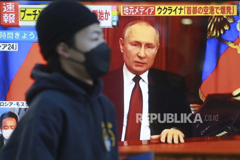 Seorang pria berjalan melewati layar TV dengan gambar Presiden Rusia Vladimir Putin di Tokyo, Kamis, 24 Februari 2022. Ketika pasukan Rusia menyerang Ukraina, para pemimpin dunia bereaksi pada Kamis dengan kemarahan, salah satu menyebutnya