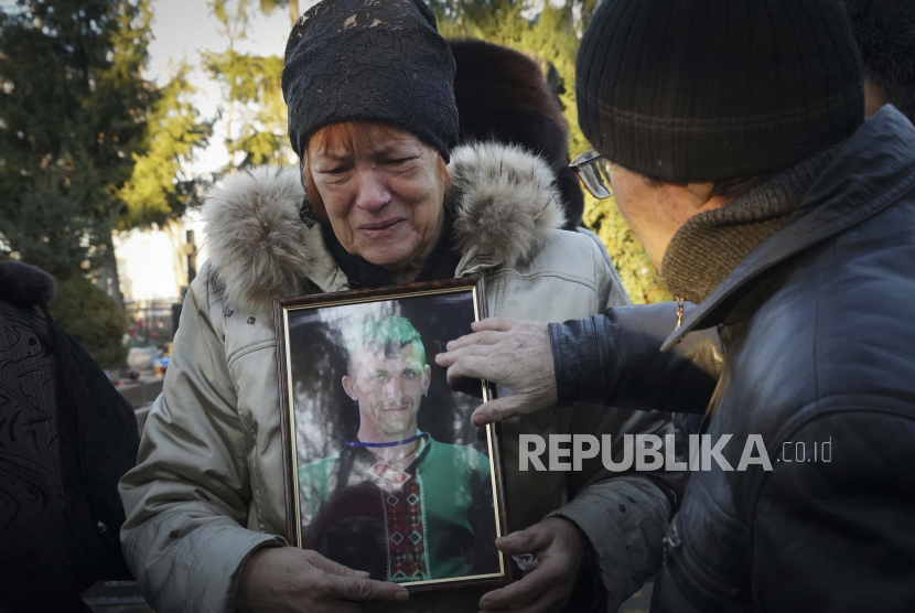 Ibu dari penulis anak-anak Ukraina Volodymyr Vakulenko memegang fotonya saat dia berduka di dekat makamnya selama upacara pemakaman di Kharkiv, Ukraina, Selasa, 6 Desember 2022. Vakulenko dibunuh oleh pasukan Rusia selama pendudukan Rusia di Izium di wilayah Kharkiv .