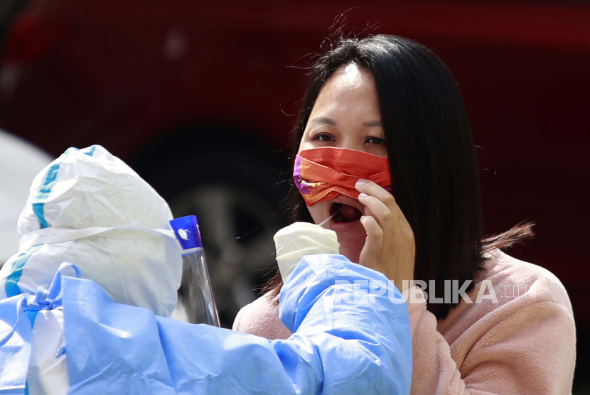 Seorang warga mengangkat maskernya untuk diambil sampelnya selama tes COVID-19 di komunitas perumahan yang dikunci di Shanghai, Cina, Rabu, 30 Maret 2022. 
