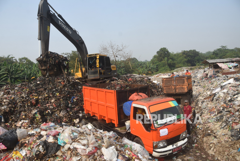 Petugas DLH (Dinas Lingkungan Hidup) menggunakan alat berat untuk mengangkut sampah. DLH Kabupaten Bekasi mengangkut sampah yang menumpuk di bahu Jalan Perjuangan.