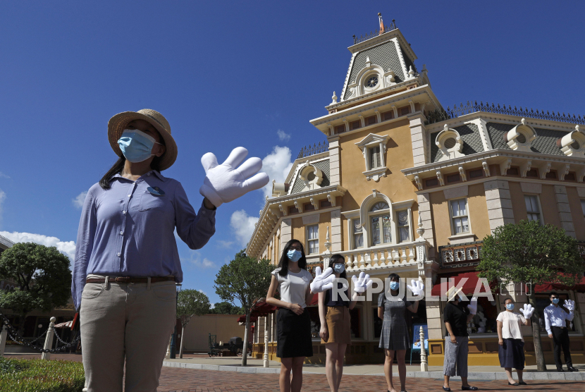 Karyawan yang memakai masker wajah untuk mencegah penyebaran coronavirus baru, menyambut pengunjung di Hong Kong Disneyland pada hari Kamis, 18 Juni 2020.