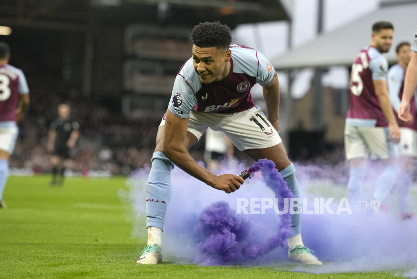 Aston Villa Ollie Watkins picks up a flare thrown onto the pitch by his teams fans after he scored his sides second goal during the English Premier League soccer match between Fulham and Aston Villa at Craven cottage stadium in London, Saturday, Feb. 17, 2024. 