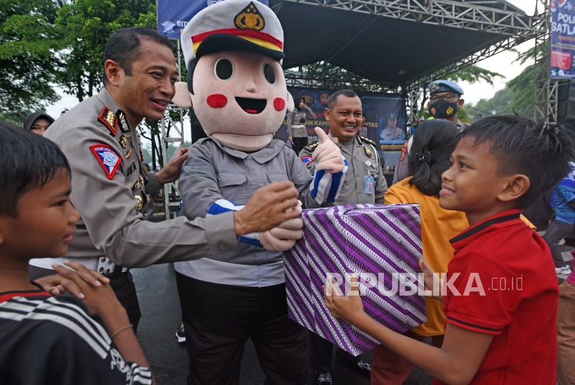 Seorang petugas keplisian didampingi Badut Lantas menyerahkan bingkisan kepada seorang anak saat mengikuti kegiatan olah raga bersama di kawasan Hari Bebas Berkendaraan di Alun-alun Serang, Banten, Ahad (3/7/2022).
