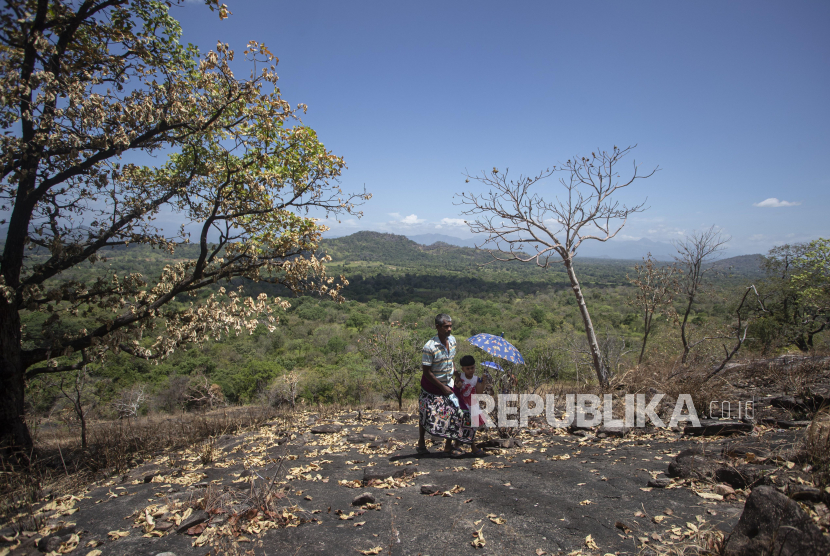 A Sri Lankan man climbs a rock in a forest reserve with a child to access the child
