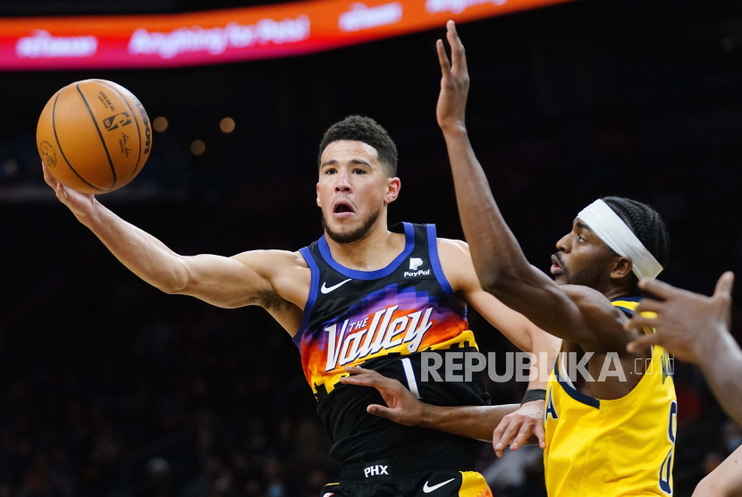 Guard Phoenix Suns Devin Booker (1) mengoper bola ke rekan setimnya saat penyerang Indiana Pacers Justin Holiday, kanan, bertahan selama paruh kedua pertandingan bola basket NBA Sabtu, 22 Januari 2022, di Phoenix.