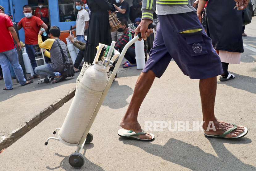 Seorang pria pergi dengan tabung oksigen penuh sementara yang lain menunggu untuk mengisi ulang tabung oksigen mereka (ilustrasi)