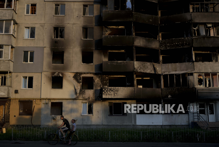 Seorang pria mengendarai sepeda di depan sebuah bangunan yang dihancurkan oleh serangan di Borodyanka, di pinggiran Kyiv, Ukraina, Ahad, 12 Juni 2022. Pergi ke Ukraina, Tiga Warga AS Dilaporkan Hilang