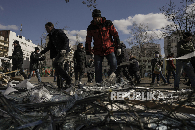 Orang-orang membersihkan puing-puing di luar pusat medis yang rusak setelah bagian dari rudal Rusia, yang ditembak jatuh oleh pertahanan udara Ukraina, mendarat di blok apartemen terdekat, menurut pihak berwenang, di Kyiv, Ukraina, Kamis, 17 Maret 2022. Satu orang dilaporkan terbunuh.