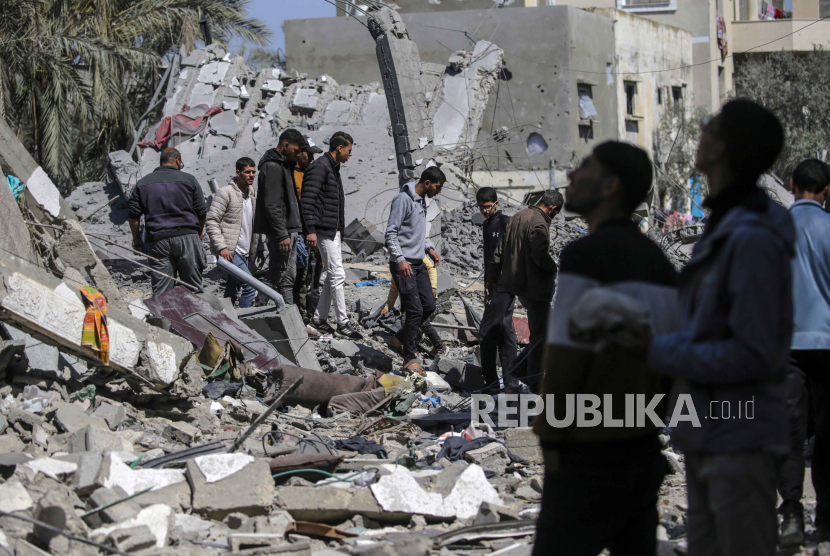 Warga Palestina menyelamatkan beberapa harta benda dan mencari orang hilang di reruntuhan rumah yang hancur menyusul serangan udara Israel di kota Deir Al Balah di selatan Jalur Gaza, (13/3/2024).