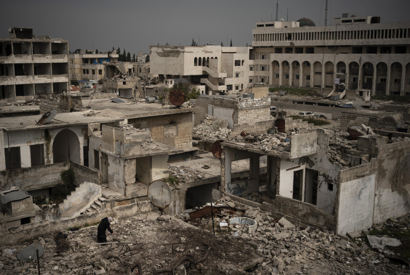 Seorang wanita berdiri diatas gedung yang hancur akibat serangan udara di kota Idlib, Suriah. (AP Photo/Felipe Dana)