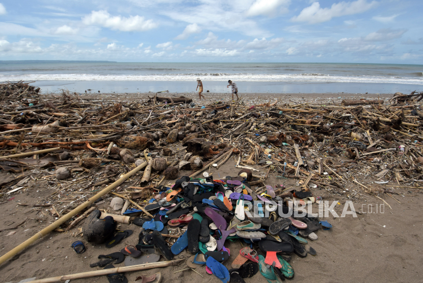 Wisatawan berjalan di dekat tumpukan sampah yang berserakan di sepanjang Pantai Berawa, Kuta Utara, Badung, Bali, Ahad (12/12/2021). Sampah tersebut terbawa arus laut yang kemudian terdampar sehingga mencemari kawasan pariwisata.