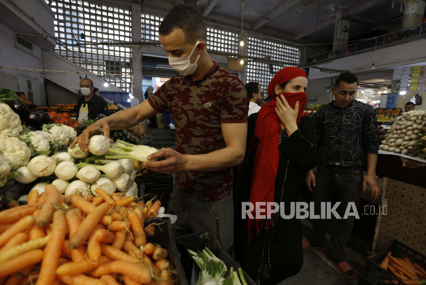 Seorang berjalan menyusuri pasar makanan sementara seorang pedagang mengenakan masker saat menata sayuran di Aljazair, Selasa (21/4). Penutupan bisnis telah secara signifikan memukul perekonomian Aljazair. Ilustrasi.