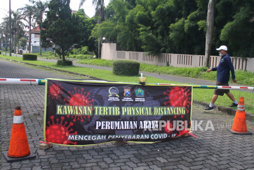 Seorang warga melintas di depan portal jalan yang ditutup di Perumahan Araya, Malang, Jawa Timur, Senin (30/3/2020). Sejumlah perumahan di kawasan tersebut mulai menutup akses jalan untuk mencegah penyebaran virus Corona