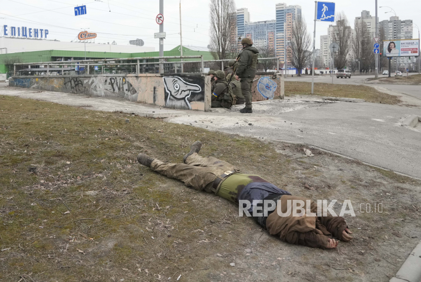  Mayat tentara yang tewas tergeletak di tanah saat tentara Angkatan Darat Ukraina duduk di sebelahnya di Kyiv, Ukraina, Jumat, 25 Februari 2022. Rusia mendesak invasi ke Ukraina ke pinggiran ibu kota setelah melancarkan serangan udara di kota-kota dan pangkalan militer dan mengirimkan pasukan dan tank dari tiga sisi.