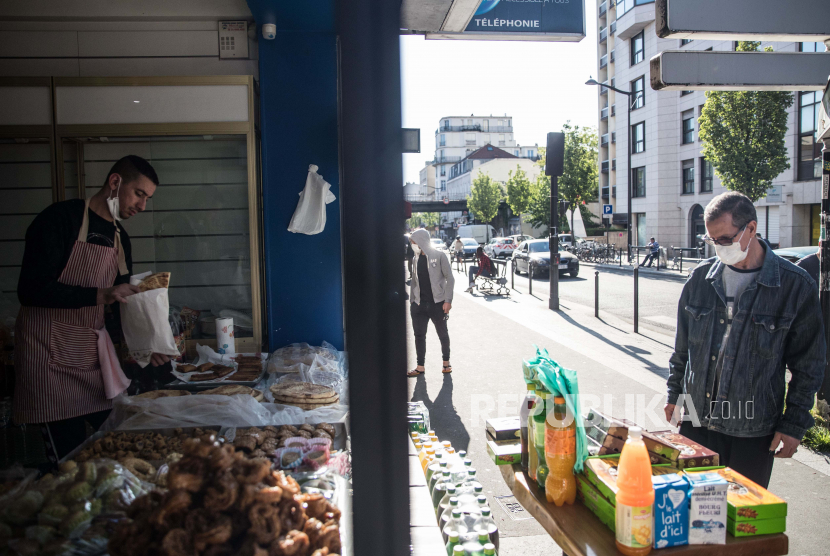 Seorang penjaga toko Aljazair dengan mengunakan masker menjual kue disaat sebelum waktu berbuka puasa di pasar Arab daerah Porte de Montreuil di Paris, Prancis, Ahad (26/4). Prancis perlu melonggarkan lockdown menghindari keruntuhan ekonomi.
