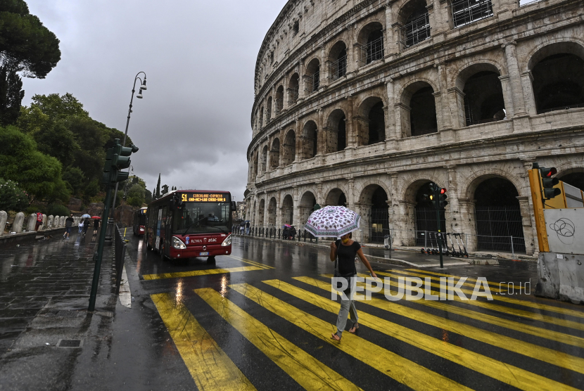 Orang-orang melewati Colosseum pada hari hujan di Roma, Italia, 31 Agustus 2020. Italia telah menyetujui paket stimulus baru untuk tahun anggaran 2021 untuk mendorong pemulihan ekonomi dari resesi yang diakibatkan krisis kesehatan pandemi Covid-19. 