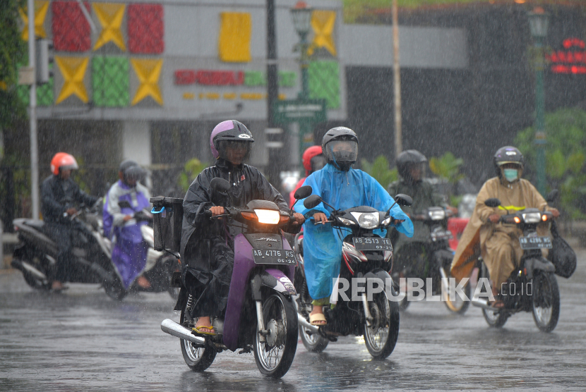 Pengendara menggunakan jas hujan menembus hujan di kawasan Tugu Pal Putih, Yogyakarta.