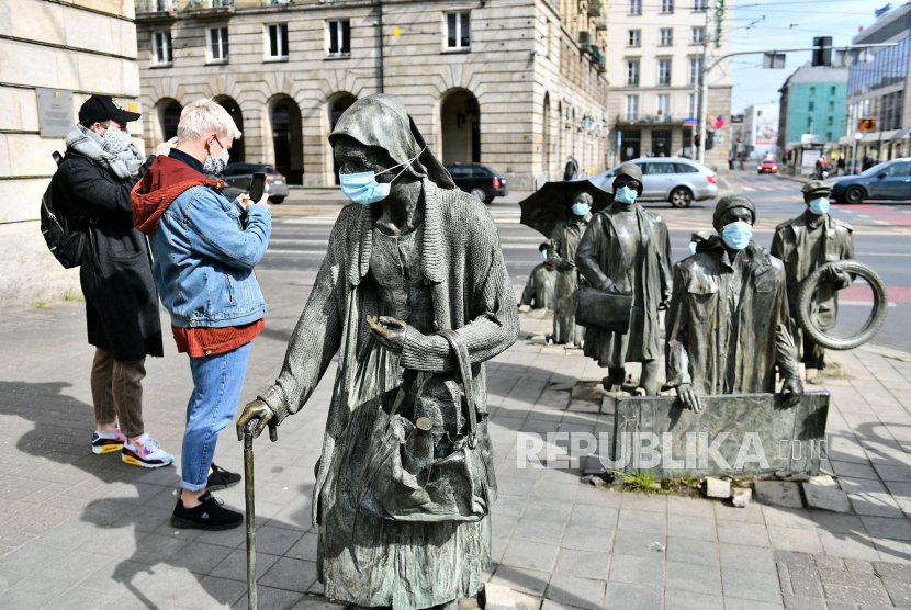 Islam di Negara Konservatif Polandia. Pengunjung mengambil foto patung Monument to Anonymous Passerby yang dipasangi masker di Wroclaw, Polandia, Rabu (15/4). Tujuan dari ini adalah untuk menyadarkan penduduk Wroclaw agar menggunakan masker sehubungan dengan pandemi virus corona
