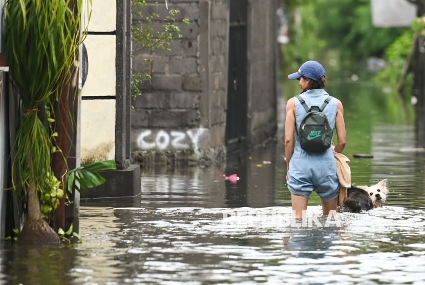 Warga bersama anjingnya berjalan menerobos banjir yang menggenangi kawasan Jalan Bumi Ayu, Sanur, Denpasar, Bali, Rabu (25/12/2024).