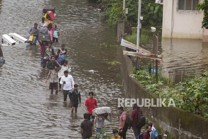 Penumpang kereta berjalan melewati genangan air di Mumbai, India, Senin (8/7/2024). 