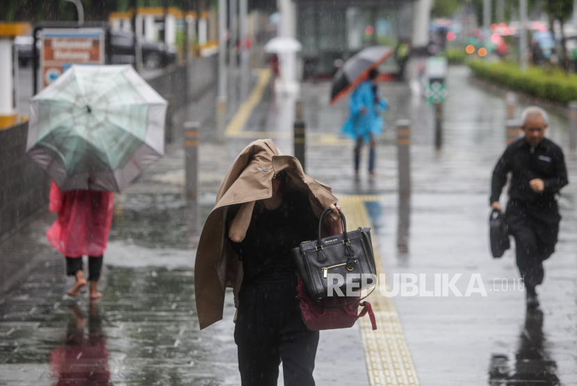 Warga melindungi kepalanya menggunakan jaket saat hujan turun di DKI Jakarta. BMKG merilis prakiraan cuaca Jakarta hari ini yang diprediksi hujan sejak pagi.