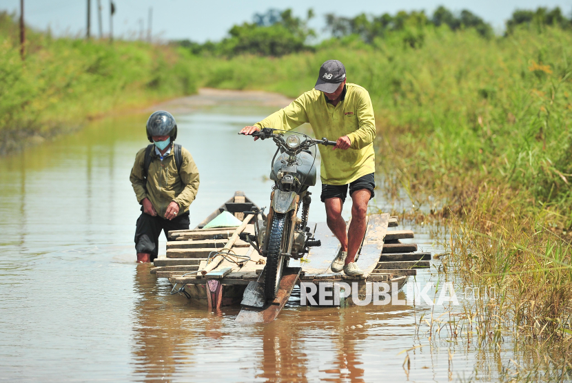 Penyedia jasa menyeberangkan pengendara sepeda motor melewati Jalan Lintas Jambi-Berbak yang terendam air di Gedong Karya, Muaro Jambi, Jambi, Ahad (8/12/2024). Banjir yang terjadi sejak seminggu terakhir akibat meluapnya air Sungai Batanghari di jalan provinsi yang menghubungkan Kabupaten Muaro Jambi dengan Tanjung Jabung Timur itu dimanfaatkan warga sekitar untuk membuka jasa penyeberangan sepeda motor dengan tarif Rp10 ribu per motor. 