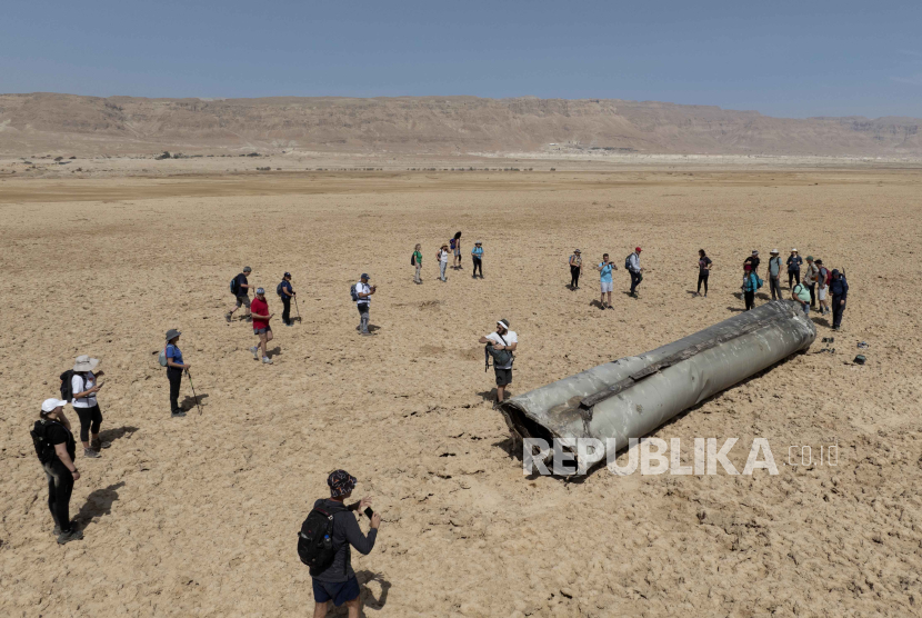 Orang-orang berkumpul di sekitar komponen rudal balistik yang dicegat yang jatuh di dekat Laut Mati di Israel, Sabtu, (20/4/2024).