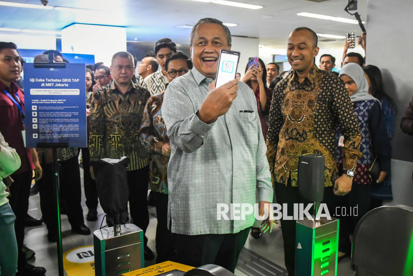 Gubernur Bank Indonesia (BI) Perry Warjiyo menunjukkan ponselnya sebelum ditempelkan ke mesin pemindai untuk membayar kereta Moda Raya Terpadu (MRT) di Stasiun MRT Bundaran HI, Jakarta, Jumat (14/3/2025). Bank Indonesia meluncurkan layanan pembayaran QRIS Tap berbasis Near Field Communication (NFC) yang memungkinkan pengguna cukup menempelkan ponsel ke mesin pemindai saat membayar belanja, KRL dan MRT sebagai inovasi untuk semakin mempermudah pembayaran digital. 