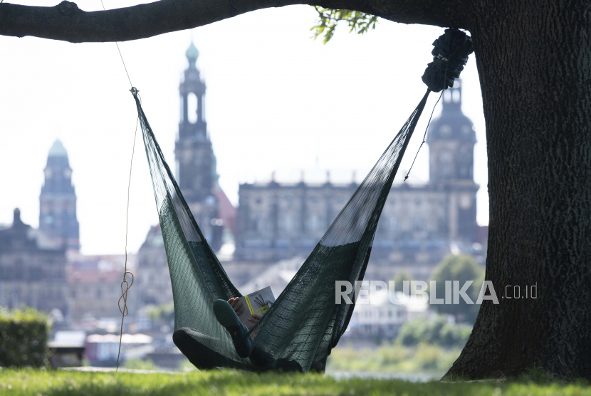  Seorang pria berbaring di tempat tidur gantung dan membaca buku di depan kota tua di Dresden, Jerman. Bloomsbury Publishing telah merevisi perkiraan keuntungannya untuk kedua kalinya tahun ini.