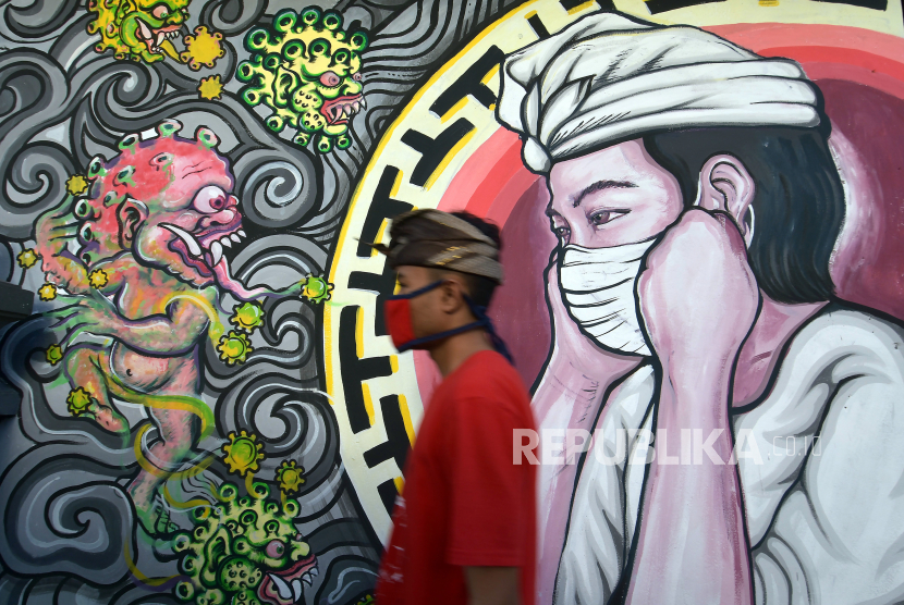 Warga melintas di dekat mural bergambar monster Covid-19 berhadapan dengan umat Hindu yang menggunakan masker di Denpasar, Bali. Satgas mencatat jumlah kasus positif secara nasional pada pekan ini jauh meningkat dibandingkan pekan sebelumnya. Satgas mencatat, terjadi peningkatan kasus positif mingguan sebesar 17,8 persen.