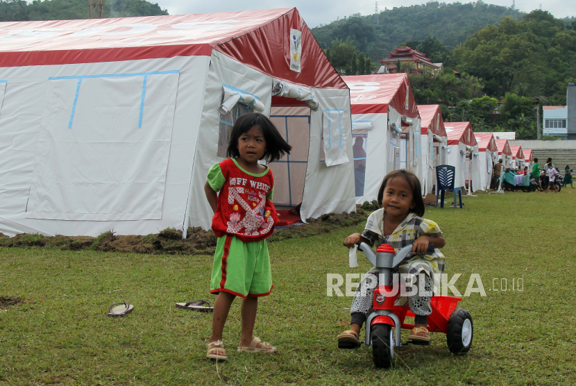 Dua anak bermain di depan tenda pengungsian , di Stadion Manakarra Mamuju, Sulawesi Barat, Ahad (24/1/2021).