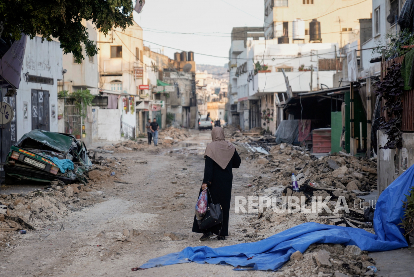 Seorang wanita Palestina berjalan di jalan yang rusak di kamp pengungsi Jenin di Tepi Barat, Rabu, 5 Juli 2023, setelah tentara Israel menarik pasukannya.